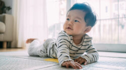 Close up of baby crawling on the floor holding themselves up and looking around.