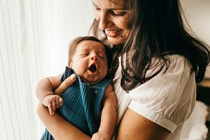 Mother holding a yawning baby next to a window.