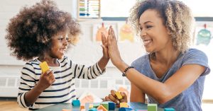 Adult and toddler high-fiving in front of a table with building blocks.