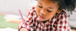 Child laying on the floor holding a pencil and writing in a notebook.