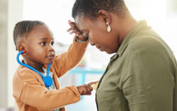 A young child wearing a toy stethoscope plays doctor, gently pressing the stethoscope to an adults chest while the adult leans in, smiling.