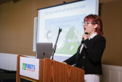 A person in a suit speaks into a microphone at a podium labeled First 5 Contra Costa, with a presentation slide titled Love on the Spectrum US displayed in the background.