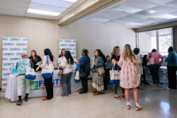 People stand in line at a registration table, receiving tote bags at an indoor event. The backdrop displays the logo First 5 Contra Costa. The atmosphere appears casual and welcoming.