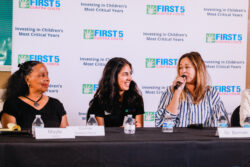 Three women sit at a table during a panel; the woman on the right speaks into a microphone. Behind them is a banner reading FIRST 5 Contra Costa and Investing in Childrens Most Critical Years..