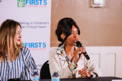 Two women sit at a table with microphones and water bottles; one woman speaks into the microphone. A First 5 Contra Costa sign is visible in the background.