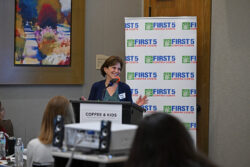 A woman speaks at a podium labeled Coffee & Kids in front of a First 5 Contra Costa banner, addressing an audience in a conference room.