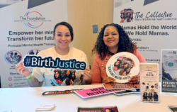 Two women sit at a table with flyers and signs promoting perinatal mental health and birth justice, smiling at the camera, supporting Black Girls Mental Health Collective.