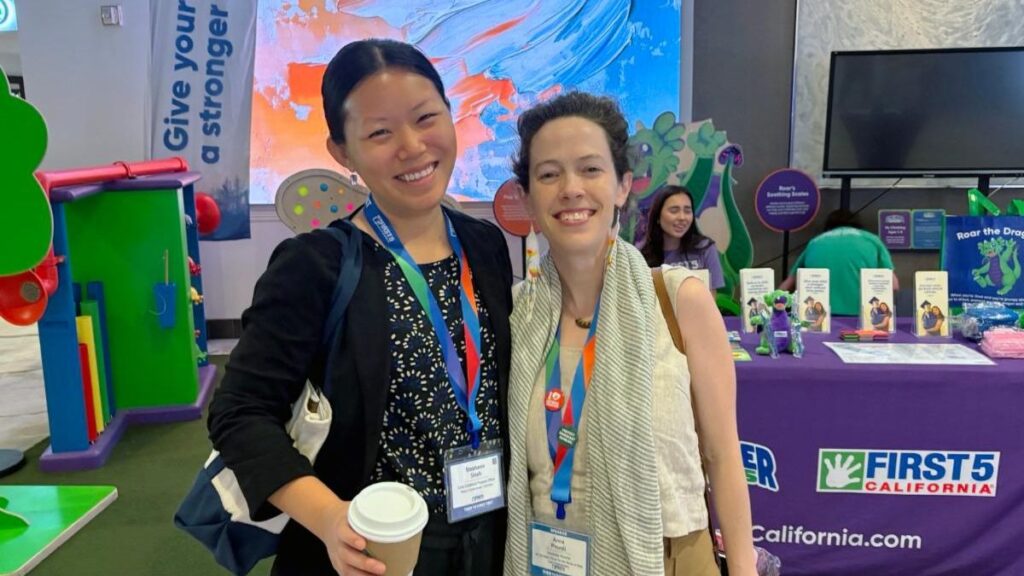 Two women posing for a photo at a First 5 California event table.