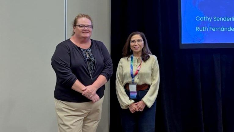 Two women standing side-by-side in front of a presentation screen.
